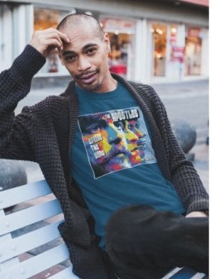 Man sitting on a city bench wearing a teal The Apostles tee under a cardigan
